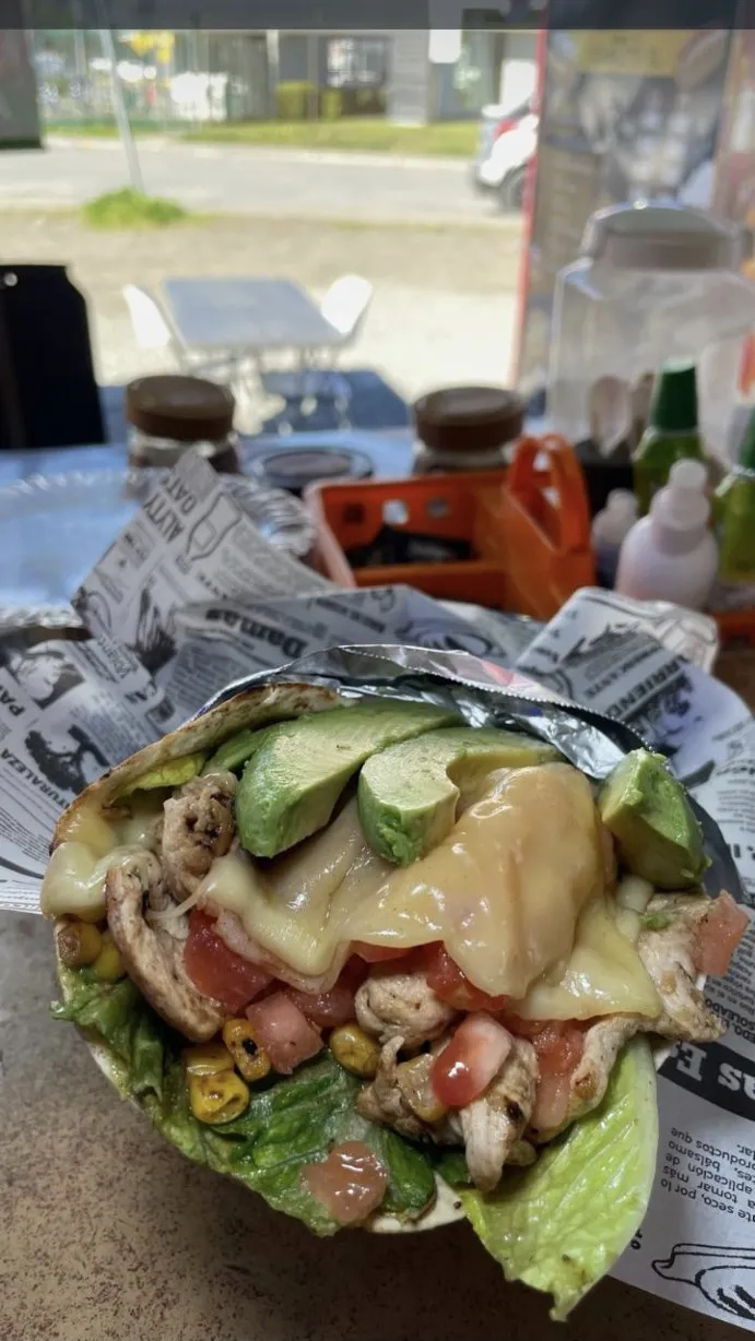 Fajita abierta con pollo, palta, queso derretido, tomate y choclo, servida sobre papel en el mesón.