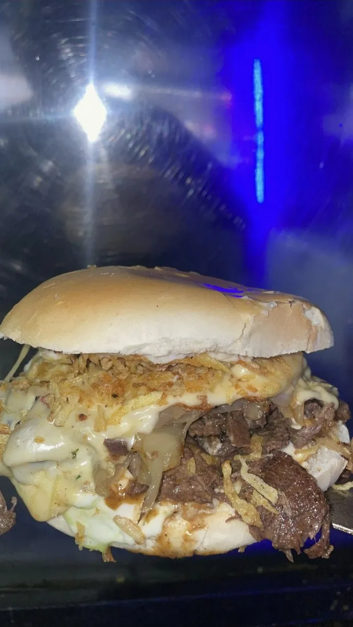 Sándwich cargado de carne, queso derretido y papas al hilo sobre la plancha.