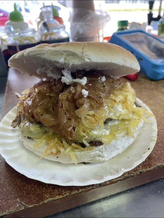 Sándwich con cebolla caramelizada, queso y papas al hilo servido en plato de cartón.